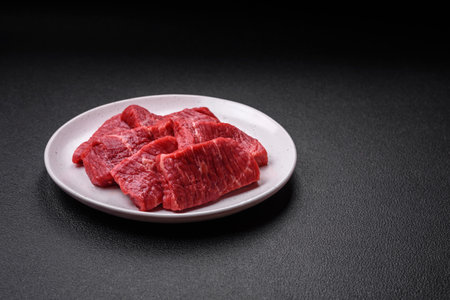 Fresh juicy raw beef slices with salt and spices on a dark concrete backgroundの写真素材