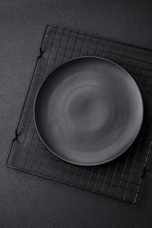 Empty ceramic round plate on dark textured concrete background. Cutlery, preparation for dinner