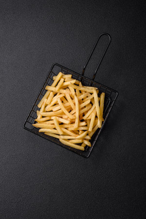 Fresh delicious crispy French fries with salt and spices on a dark concrete background
