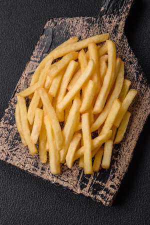 Fresh delicious crispy French fries with salt and spices on a dark concrete background