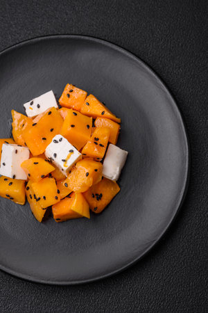 Delicious juicy salad of diced grilled pumpkin with feta cheese, spices and sesame seeds on a ceramic plateの写真素材