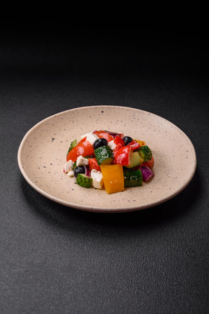Delicious juicy Greek salad with feta cheese, olives, cucumber and tomatoes on a ceramic plate on a dark concrete backgroundの写真素材