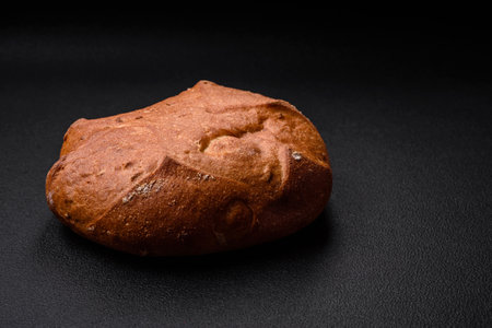Delicious fresh crispy brown bread with seeds and grains on a dark concrete background
