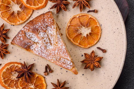A piece of baked homemade pie with apple or pear, with cinnamon, sprinkled with powder on a dark concrete backgroundの写真素材