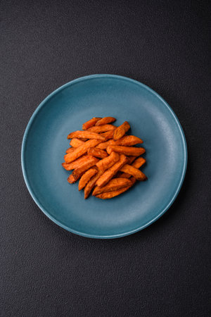 Delicious crispy sweet potato fries with salt, spices and herbs on a dark concrete backgroundの写真素材