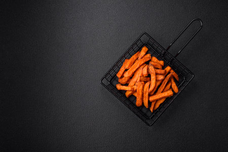 Delicious crispy sweet potato fries with salt, spices and herbs on a dark concrete backgroundの写真素材