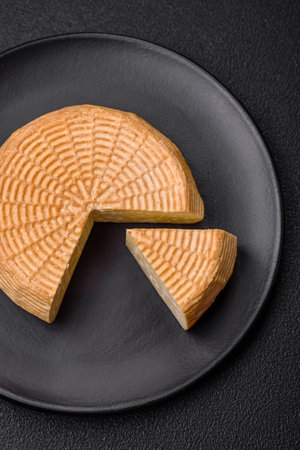 Delicious hard craft cheese made from cow or goat milk on a dark concrete background