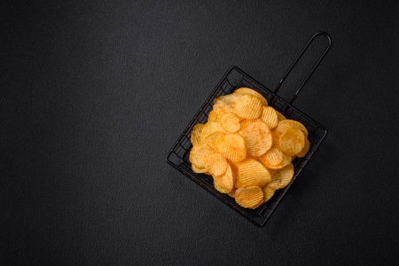 Crispy potato chips with salt, spices and herbs on a dark concrete background