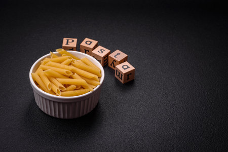 Raw penne pasta from whole grain wheat varieties with salt and spices on a dark concrete backgroundの写真素材
