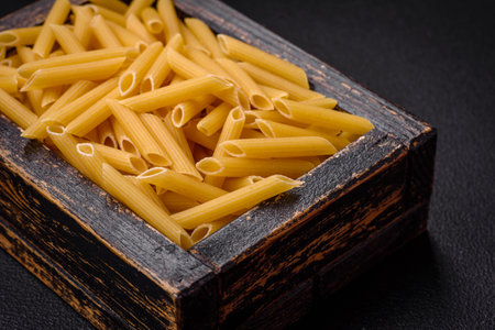 Raw penne pasta from whole grain wheat varieties with salt and spices on a dark concrete backgroundの写真素材