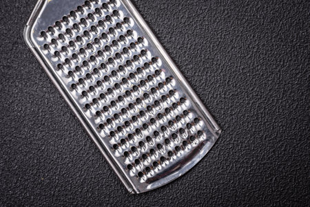 Beautiful small metal kitchen grater with handle on a dark textured backgroundの写真素材