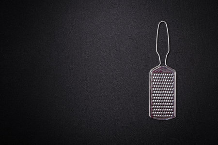 Beautiful small metal kitchen grater with handle on a dark textured backgroundの写真素材