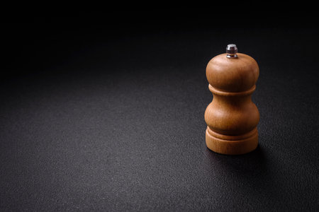Beautiful wooden figured pepper shaker or salt shaker with a mill on a dark textured backgroundの写真素材