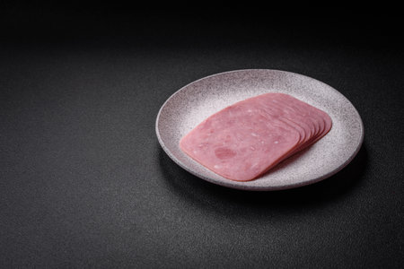 Delicious fresh ham cut into slices with salt, spices and herbs on a dark concrete backgroundの写真素材