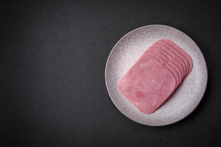 Delicious fresh ham cut into slices with salt, spices and herbs on a dark concrete backgroundの写真素材