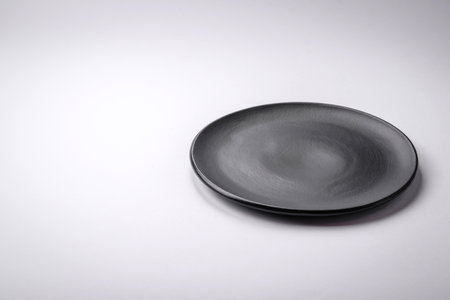 Empty round ceramic plate on a plain background, flatley with copy space. Kitchen utensils in home...