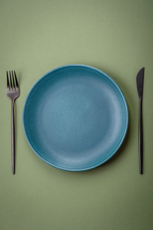 Empty round ceramic plate on a plain background, flatley with copy space. Kitchen utensils in home...