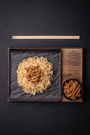 Delicious Asian cuisine dish with rice noodles, peppers, mushrooms and spices on a dark concrete...