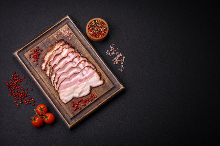 Delicious fresh pancetta or bacon with salt and spices cut into thin slices on a dark concrete...