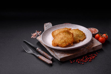 Delicious crispy pancakes made from potatoes, meat, carrots, onions with salt, spices and herbs on a dark concrete backgroundの写真素材