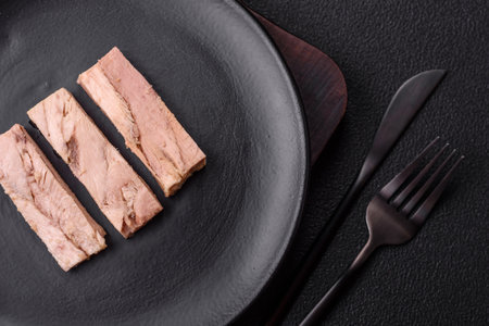 Delicious canned dietary tuna meat with salt, spices and oil on a dark concrete background