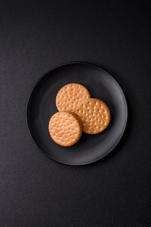 Round dotted snack snack cookies with cream on a dark concrete background. Sweets for breakfastの写真素材