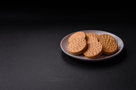 Round dotted snack snack cookies with cream on a dark concrete background. Sweets for breakfastの写真素材