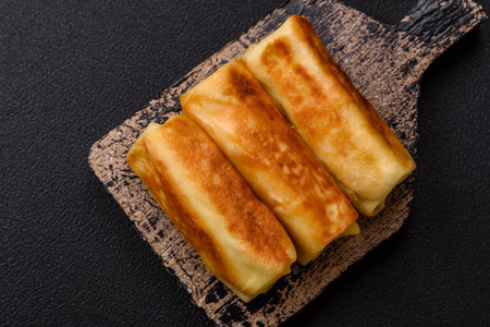 Delicious fried pancakes with filling rolled on a dark concrete background. Delicious nutritious breakfastの写真素材