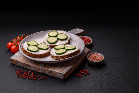 Delicious vegetarian sandwich with grilled toast, cream cheese, cucumbers and seeds and grains on a dark concrete backgroundの写真素材