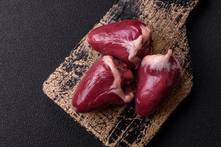Raw turkey or chicken hearts with salt and spices on a dark concrete background