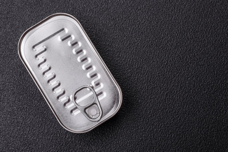 Rectangular can of fish in oil with salt and spices on a dark concrete background