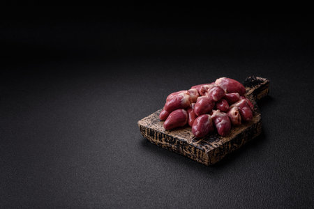 Raw chicken hearts with salt, spices and herbs on a dark concrete background
