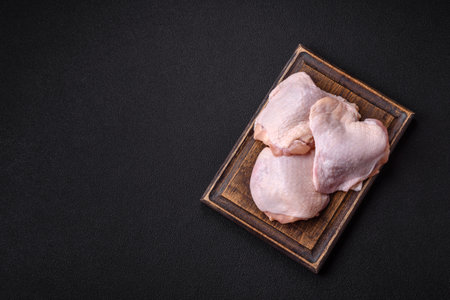 Fresh raw chicken thighs with salt and spices on dark concrete backgroundの写真素材