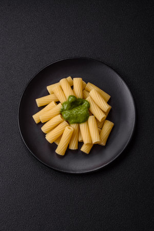 Delicious pasta with spinach sauce, olive oil and parmesan cheese with salt, spices and herbs on a dark concrete backgroundの写真素材