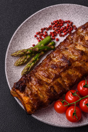 Delicious juicy grilled ribs with honey and mustard sauce with salt, spices and herbs on a dark concrete backgroundの写真素材