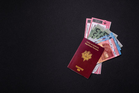 Passport of the Republic of France, airline tickets and money on a dark concrete background....