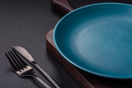 Empty ceramic round plate on dark textured concrete background. Cutlery, preparation for dinnerの写真素材