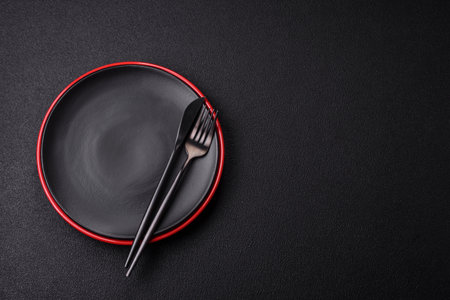 Empty ceramic round plate on dark textured concrete background. Cutlery, preparation for dinnerの写真素材