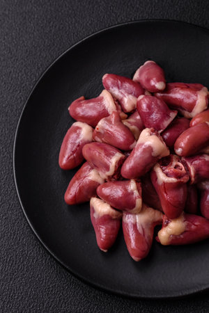 Raw chicken hearts with salt, spices and herbs on a dark concrete backgroundの写真素材