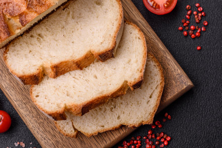 A loaf of brown bread with grains of cereals on a wooden cutting board on a dark concrete background