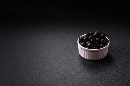 Ripe blackcurrant berries in droplets of water in a ceramic bowl on a dark concrete background