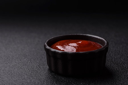 Delicious spicy tomato sauce with pepper, garlic, salt, spices and herbs in a white gravy boat on a dark concrete backgroundの写真素材