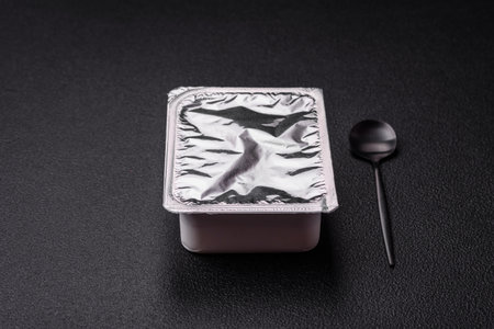 Rectangular plastic box with yogurt or cheese hermetically sealed with a foil lid on a dark concrete...