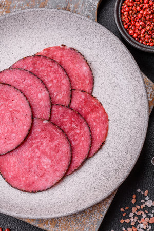 Delicious smoked salami sausage sliced with salt, spices and herbs on a dark concrete backgroundの写真素材