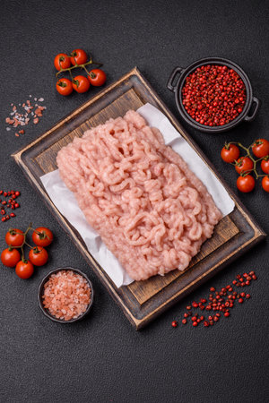 Fresh raw chicken mince with salt and spices on a dark concrete background