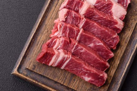Fresh raw beef cut into slices with salt, spices on a dark concrete background