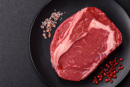 Fresh, raw beef steak with salt, spices and herbs on a dark textured backgroundの写真素材