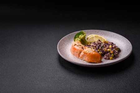 A piece of salmon with rice, broccoli, salt and spices on a dark concrete backgroundの写真素材