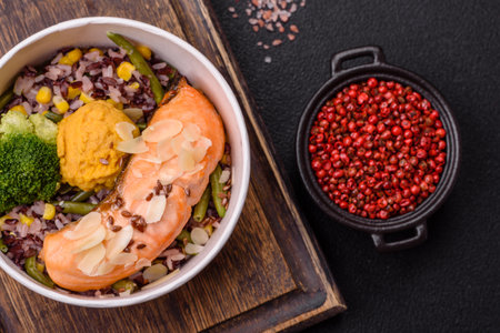 A piece of salmon with rice, broccoli, salt and spices on a dark concrete backgroundの写真素材