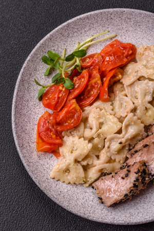 Bowl with slices of baked tuna with broccoli, tomatoes and fusili pasta, with salt and spices on dark concrete backgroundの写真素材